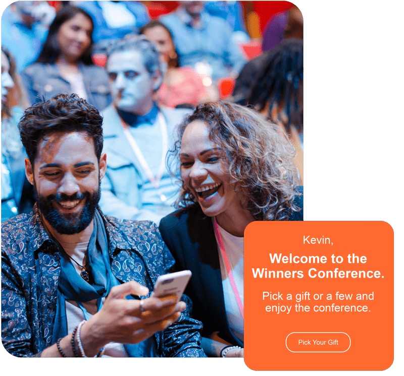 Two people smile at a phone, exploring an event gifting solution while seated at a conference. Two people smile at a phone, exploring an event gifting solution while seated at a conference.